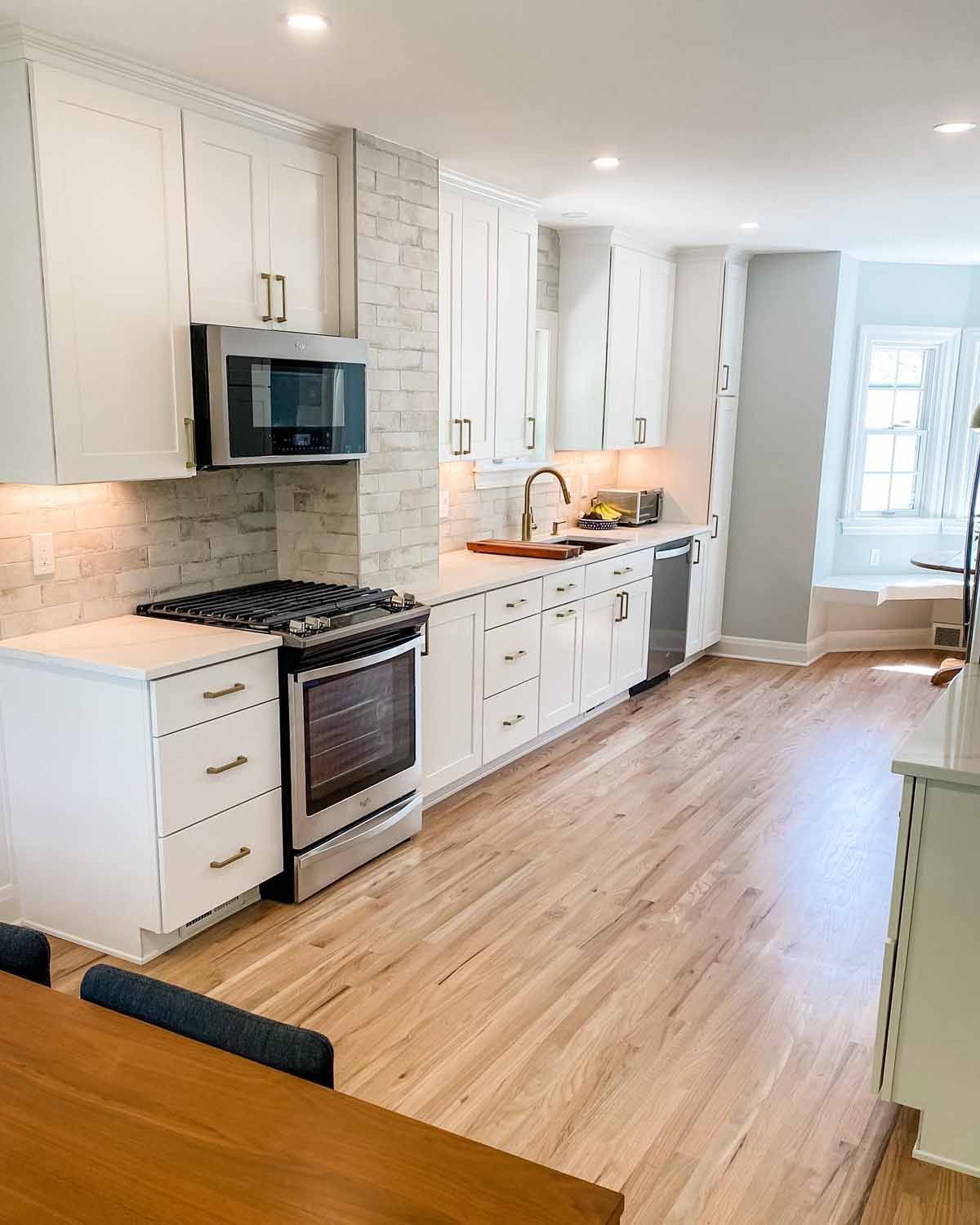 White kitchen with wooden floors, stainless steel appliances, and brick backsplash.