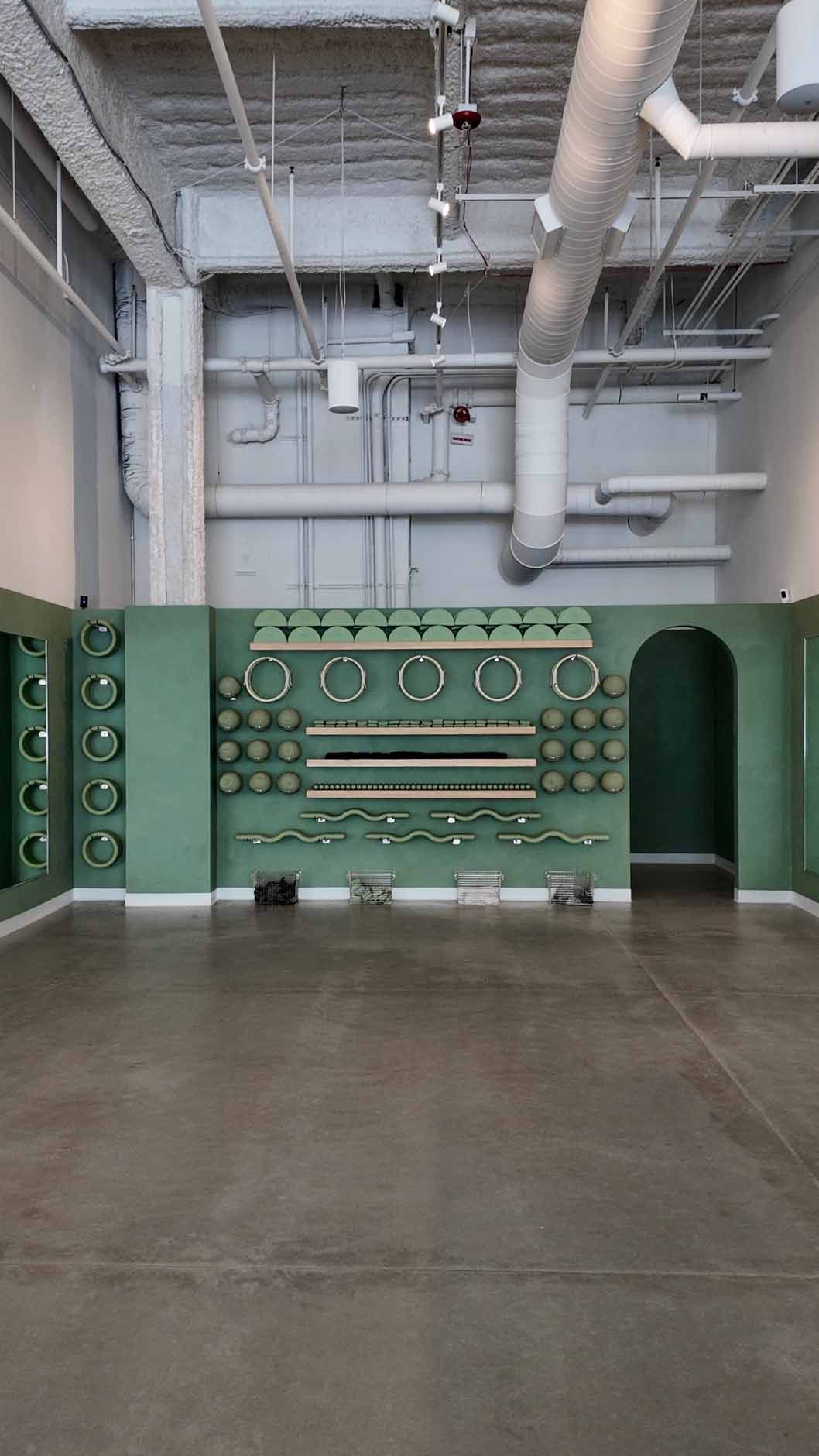 A green wall with clocks and arched doorway in a large, empty room.