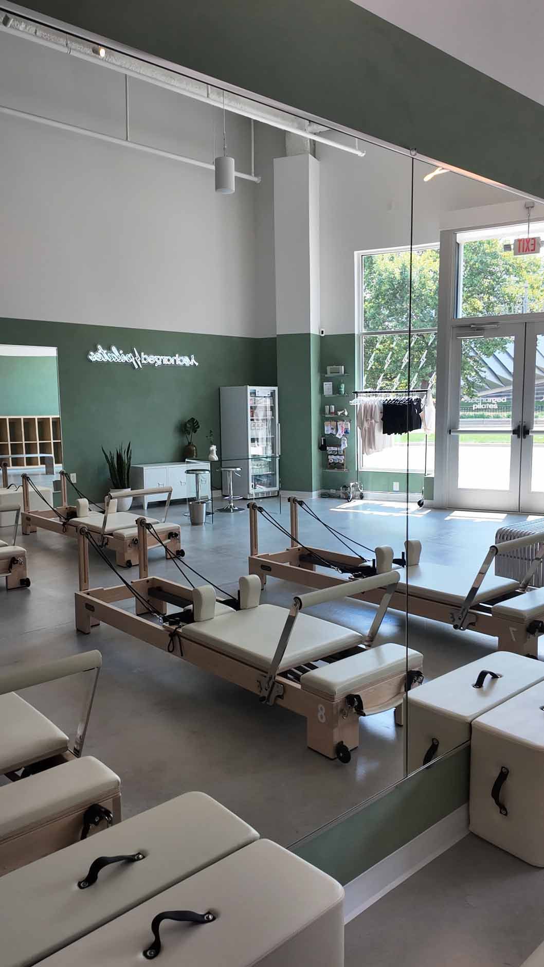 Pilates studio interior with exercise machines, light wood, green accents, and large windows.