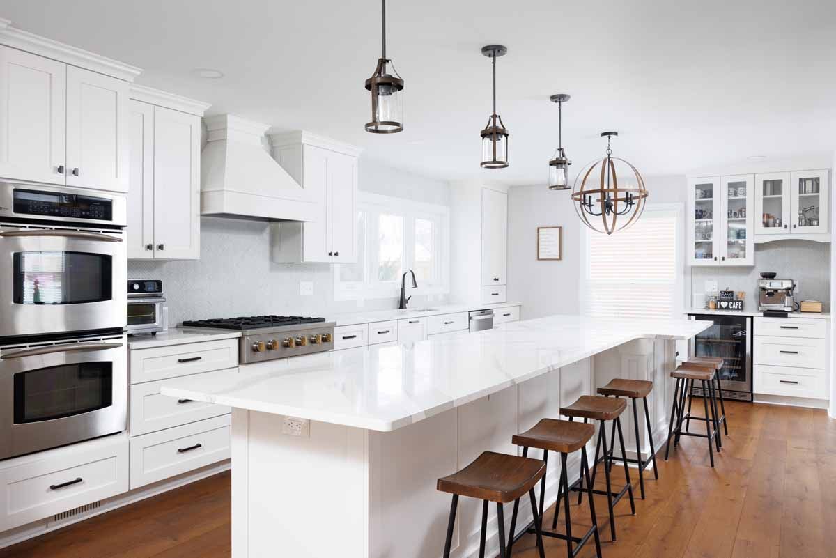 White kitchen with island seating, stainless steel appliances, and pendant lights.