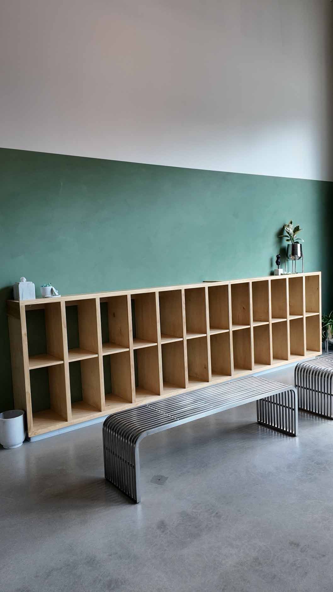 A long, light-wood cubby shelf against a green wall, with two benches in front.