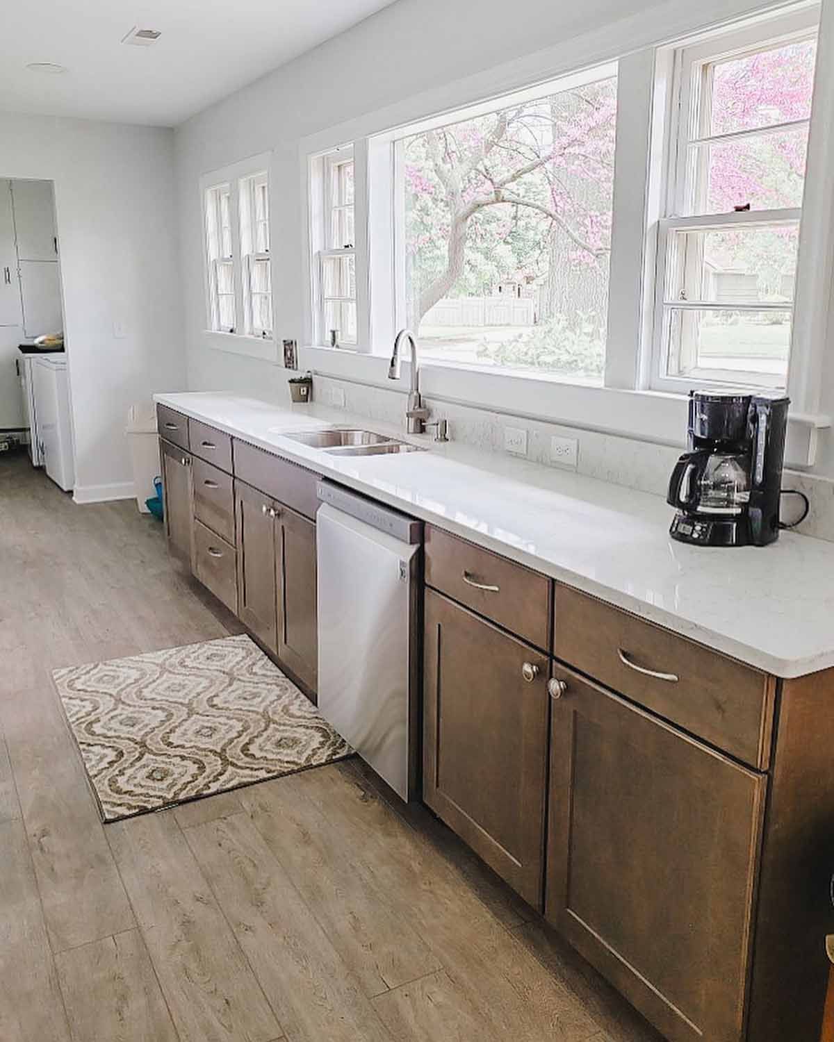 Kitchen with brown cabinets, white countertops, sink, and windows overlooking a tree with pink flowers.