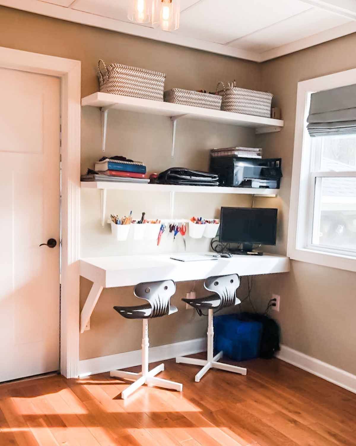 A home office with a white desk and shelves, two chairs, a printer, and baskets, in a room with a window.