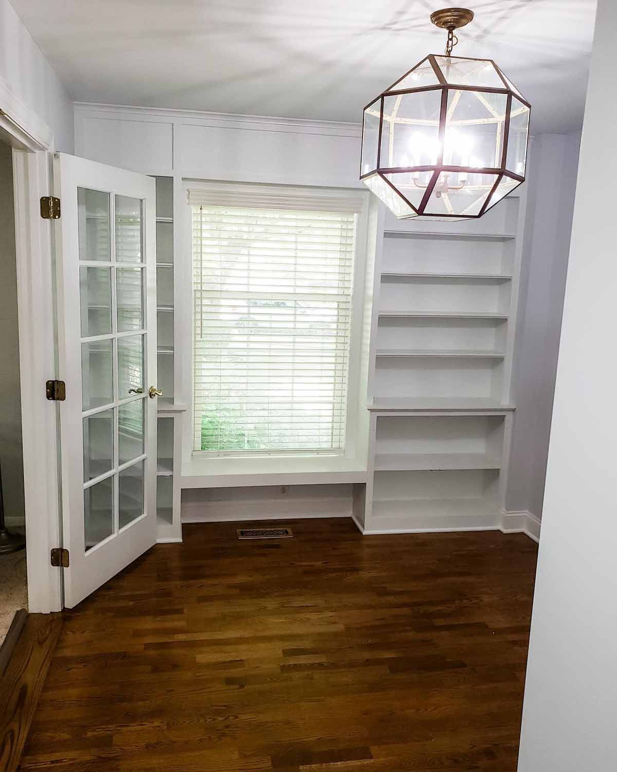 Room with built-in bookshelves, French doors, wood floor, and decorative geometric light fixture.