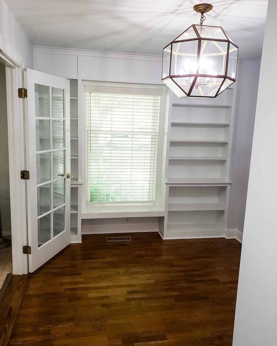 Room with built-in bookshelves, French doors, wood floor, and decorative geometric light fixture.