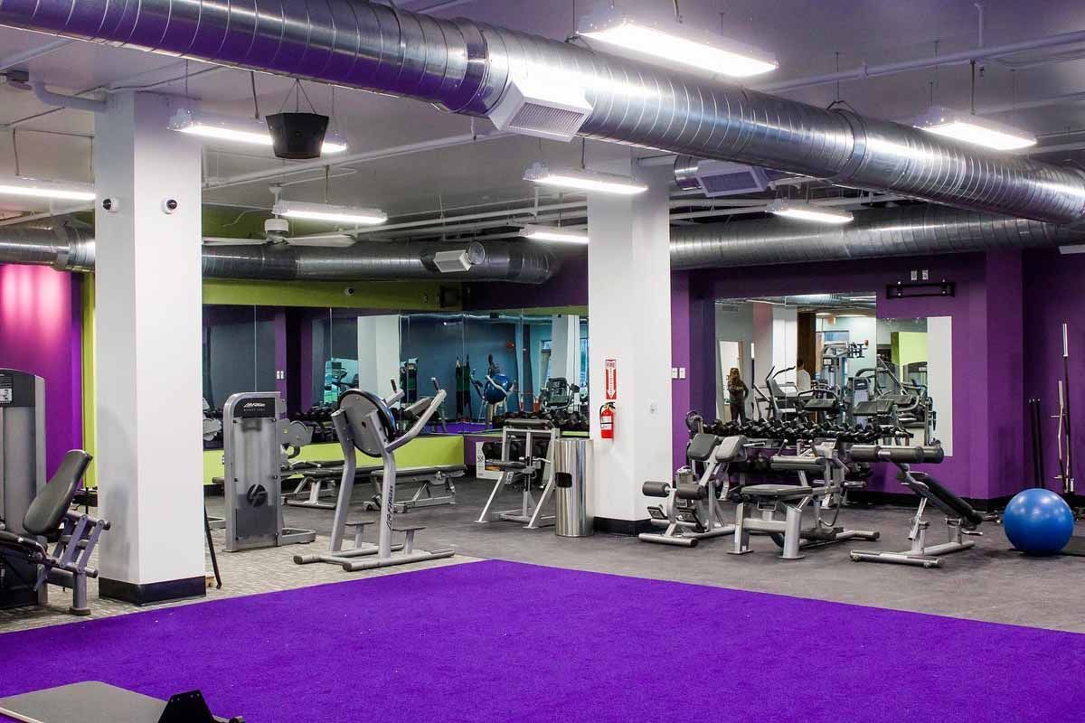 Gym interior with purple floor, workout machines, mirrored walls, and a blue exercise ball.