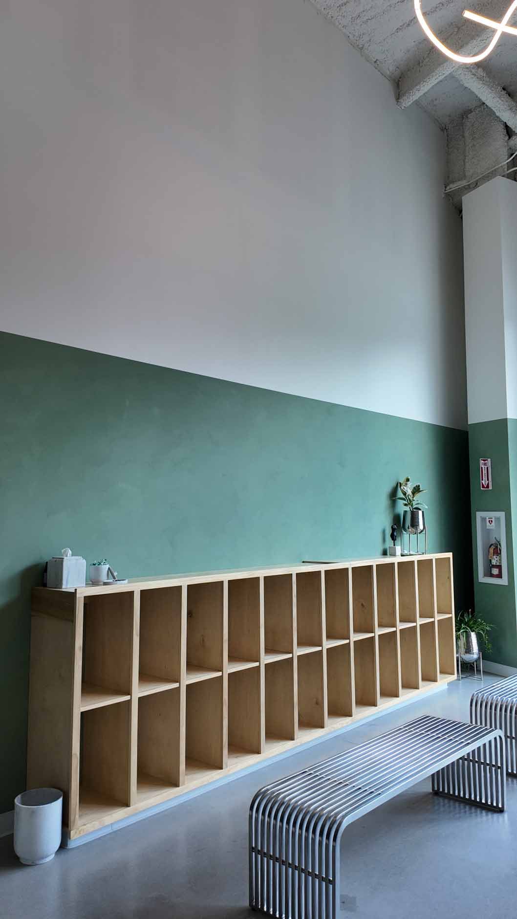 Long wooden shelving unit with a bench, against green and white painted wall.
