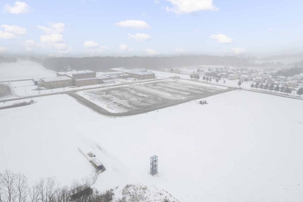 Snowy field and buildings under a cloudy sky; a town in the background.