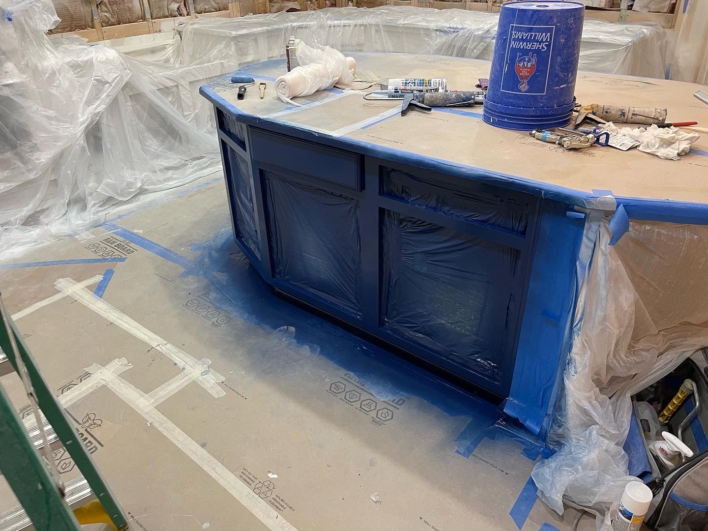A partially painted blue cabinet being spray-painted in a construction setting.