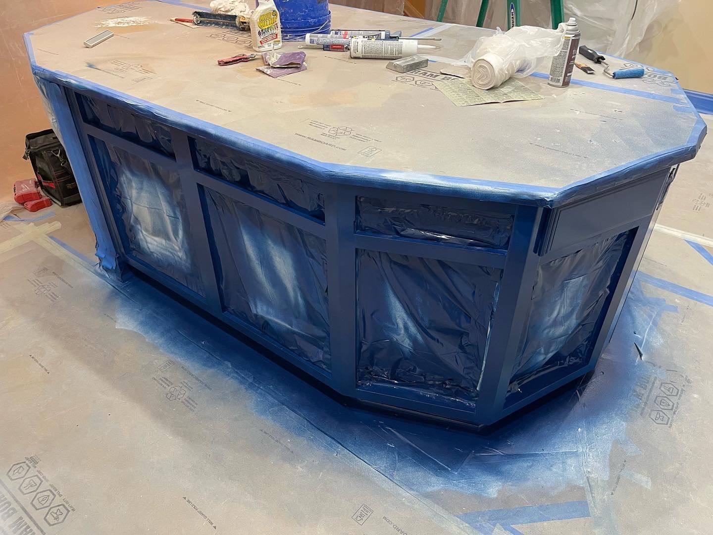 Blue painted kitchen island, being painted with tape and plastic covering areas.