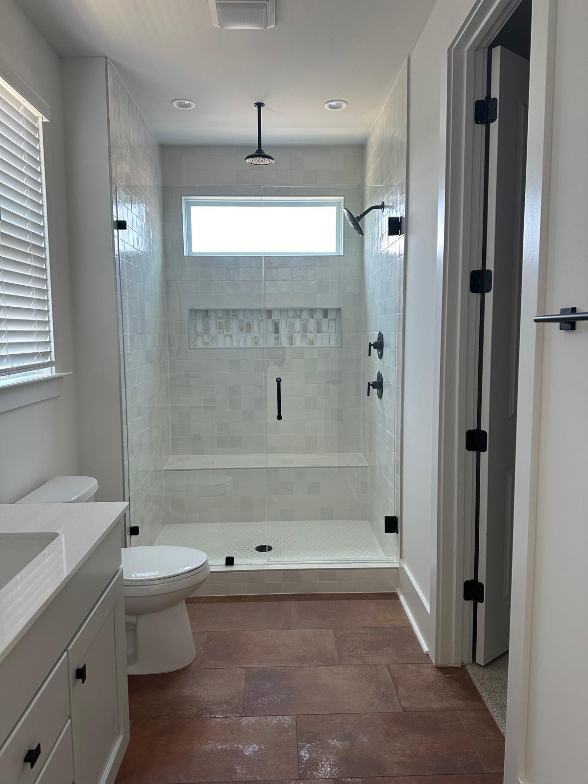 Bathroom with glass shower, white walls, wood-look floor, toilet, and vanity.