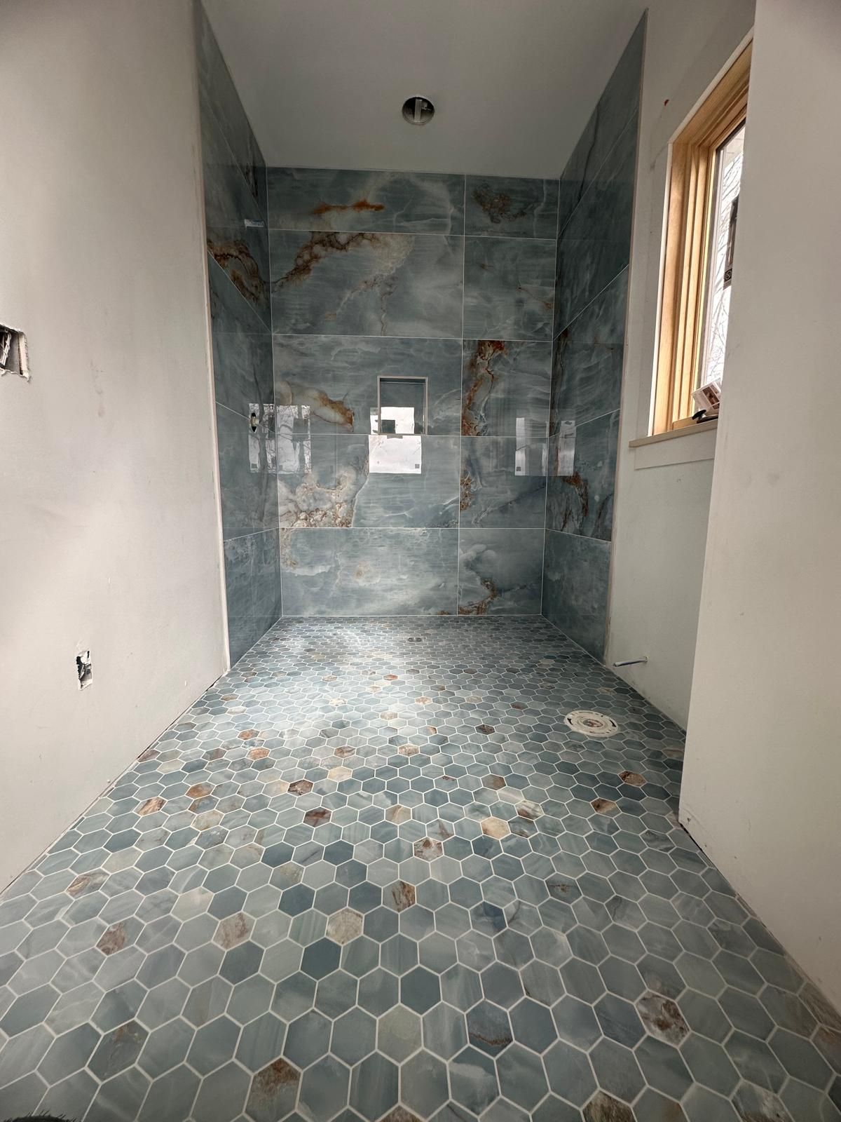 Bathroom under construction with blue and brown tiles and a window.