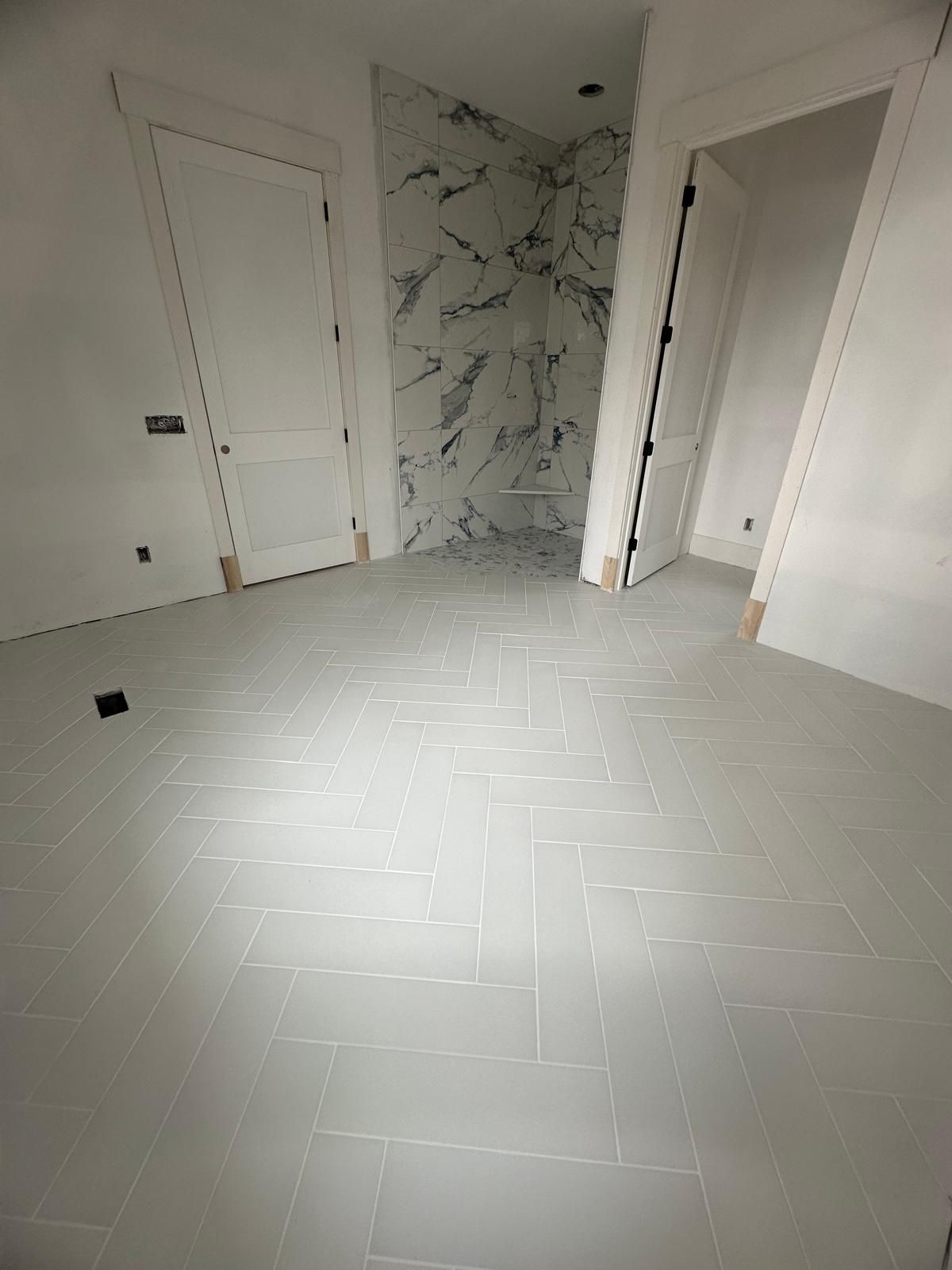 A room with gray tiled floor, two white doors, and a shower with marble-look walls.