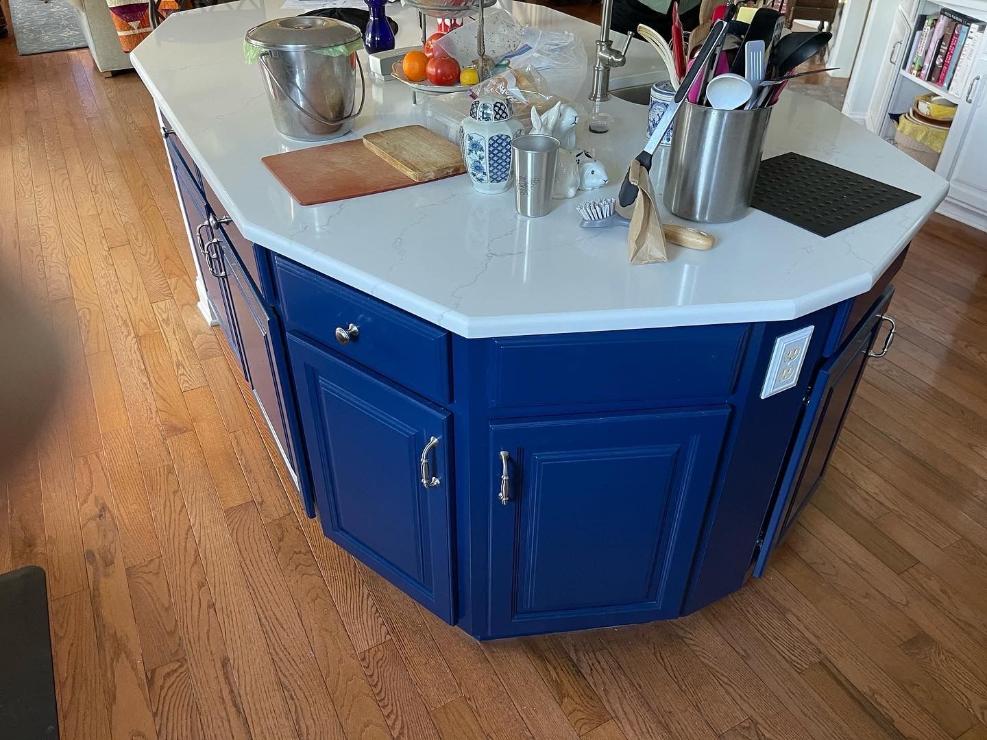 Blue kitchen island with a white countertop, on a hardwood floor.