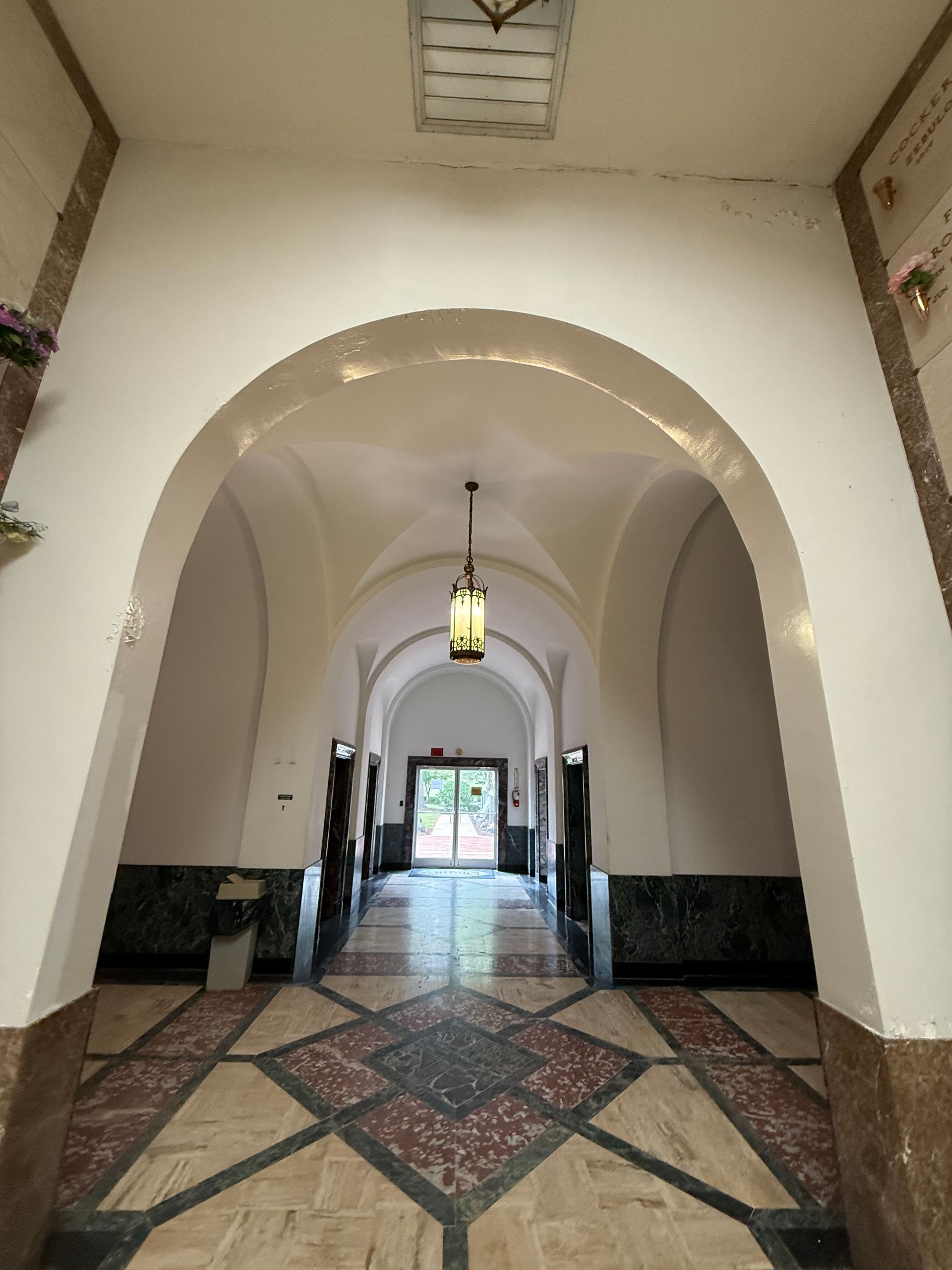 Hallway in mausoleum with arched ceilings, ornate floor, and a hanging light.