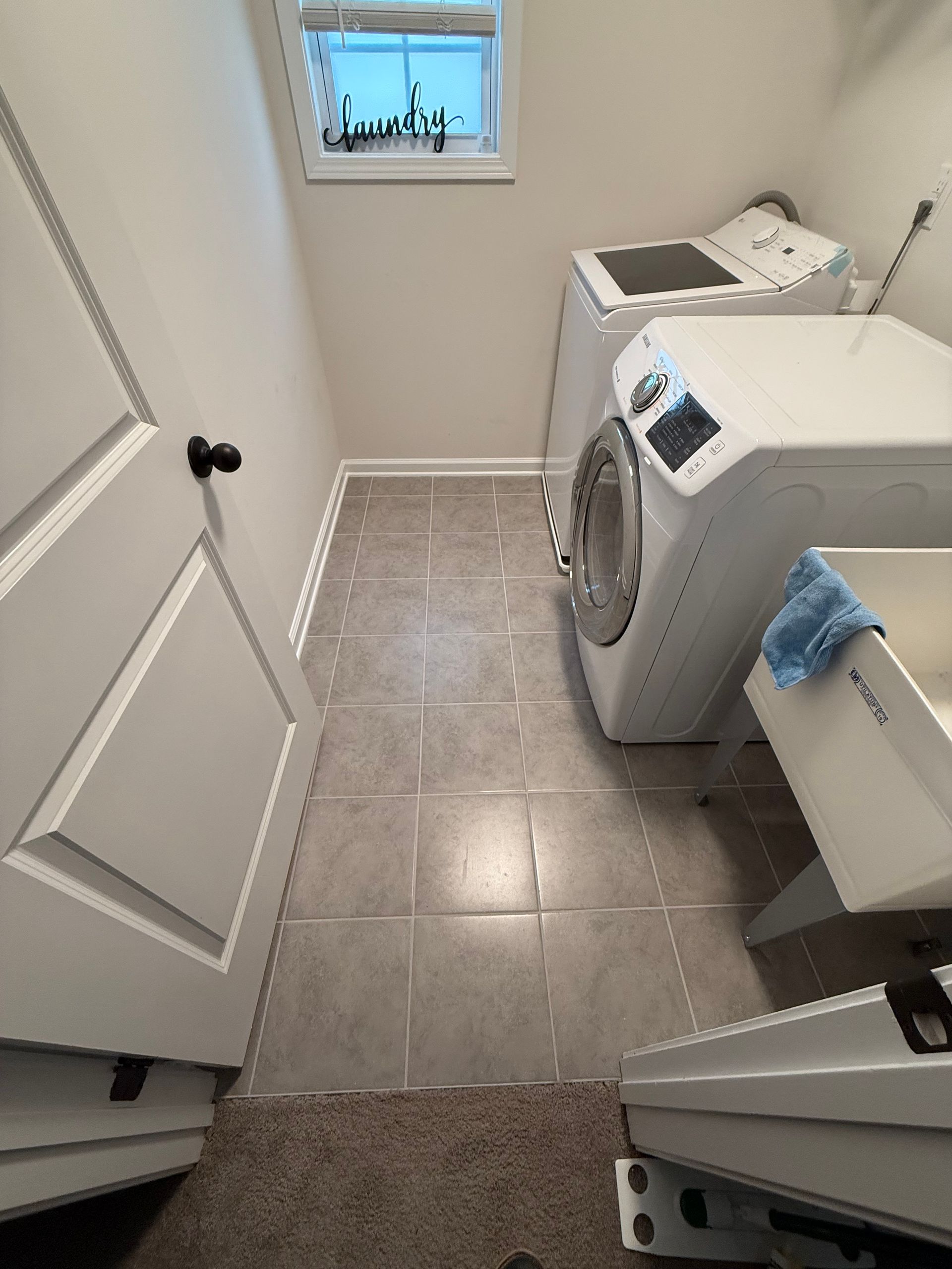 Laundry room with washing machine, tiled floor, window, and open door.