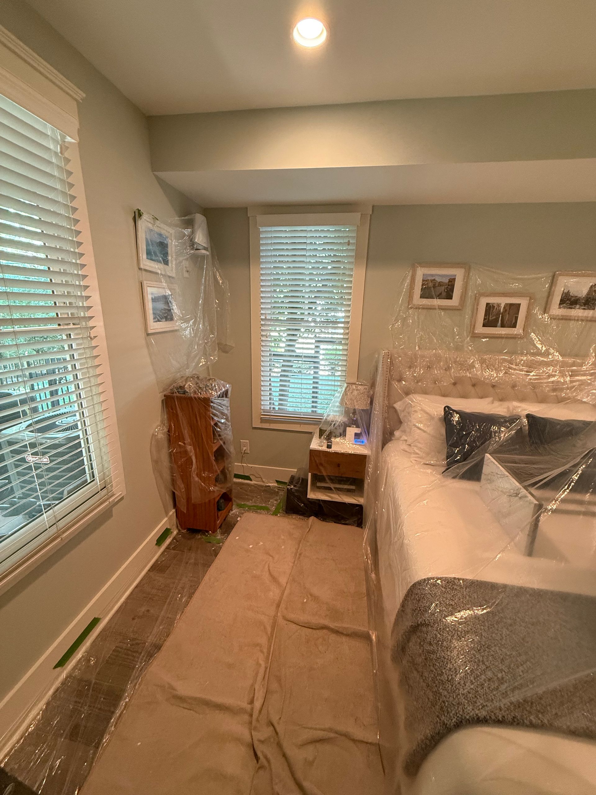Bedroom with furniture covered in plastic for protection during painting.