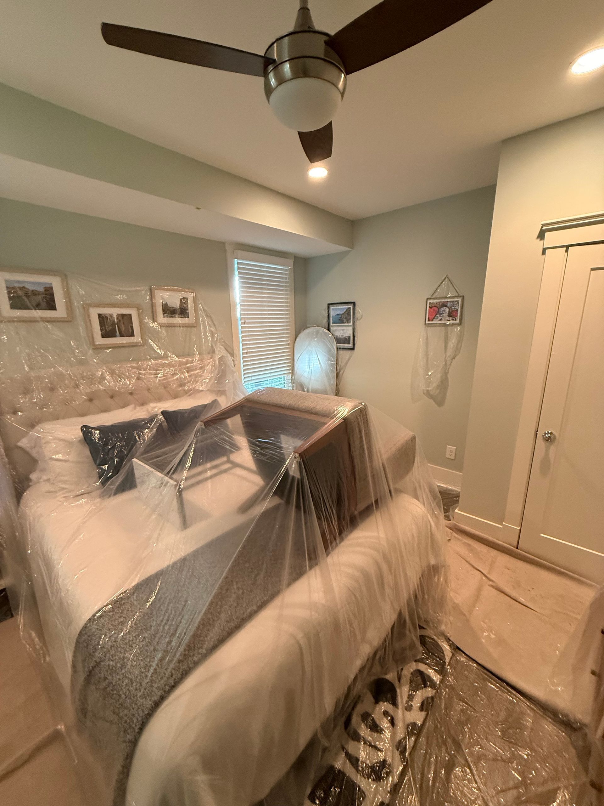 Bedroom wrapped in plastic for protection during renovation. Includes a bed, ceiling fan, and closed door.
