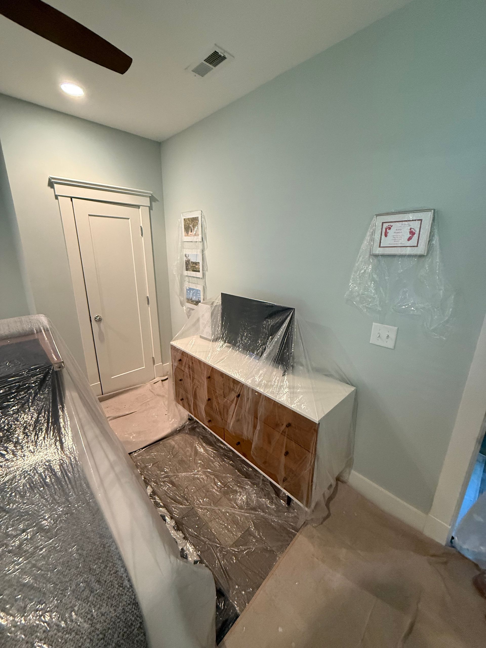 Room with a TV on a white and wood cabinet, light blue walls, and a door.