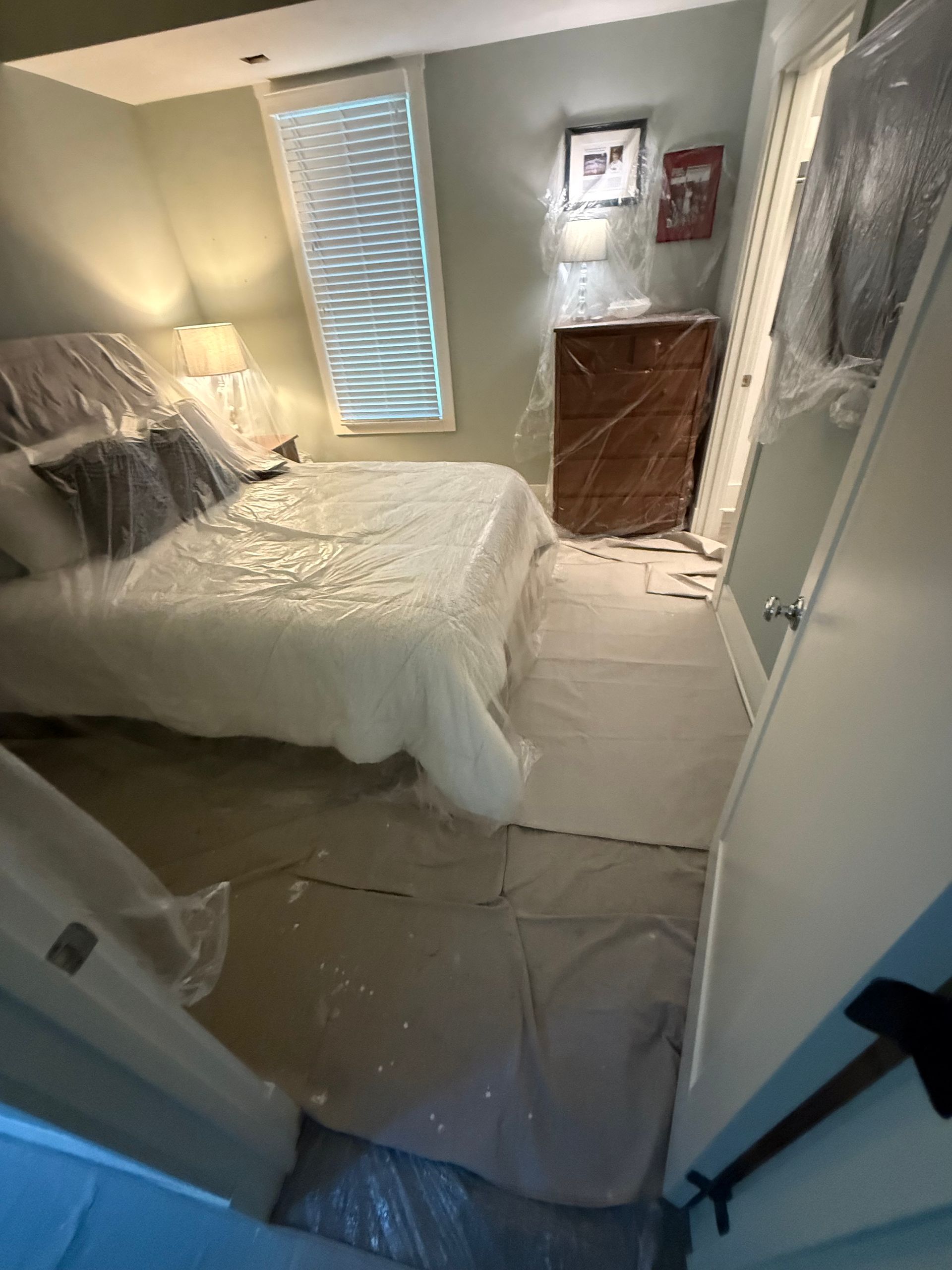 Bedroom protected with plastic sheeting for painting or renovation. Bed and dresser covered.