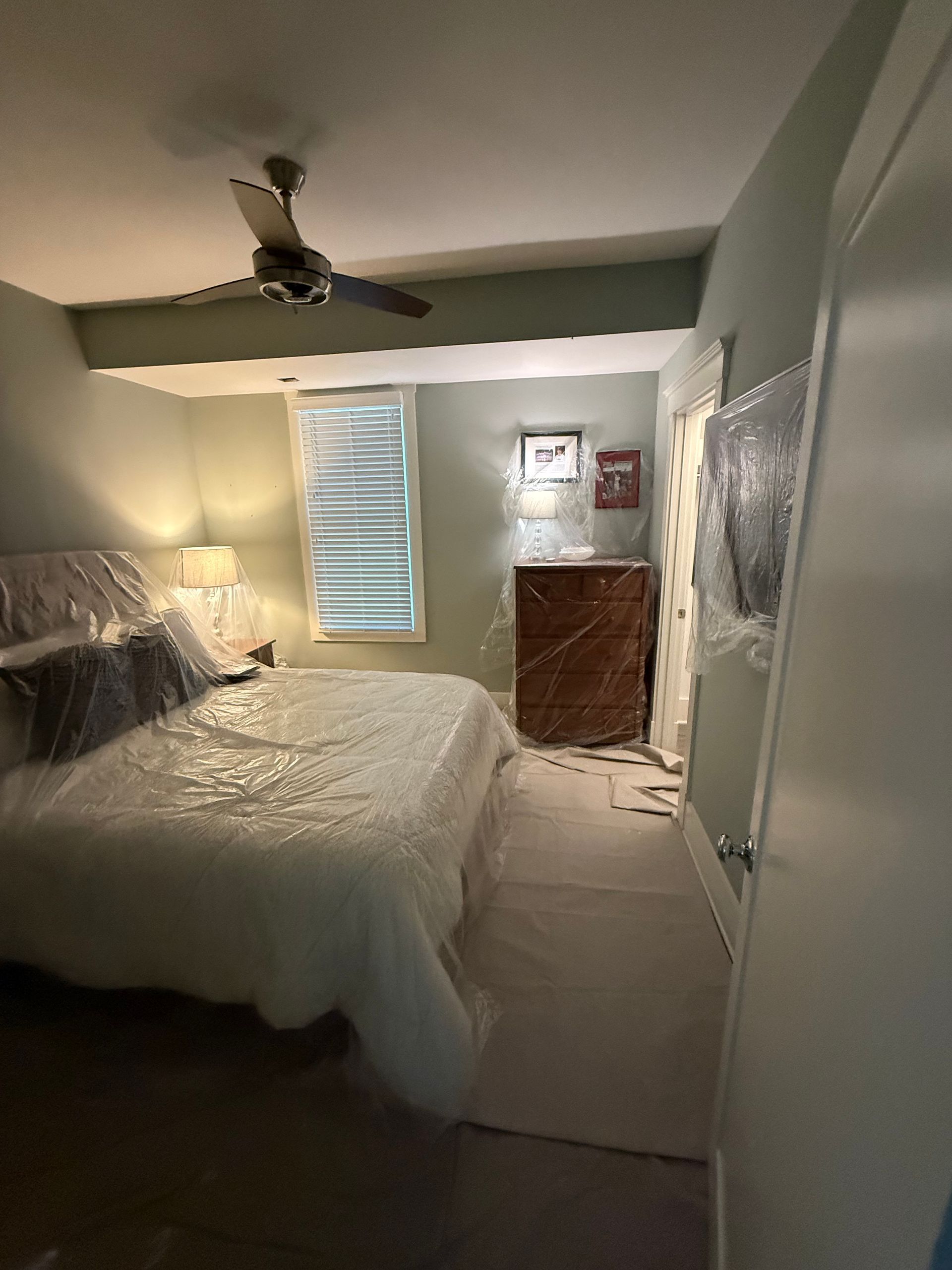 Bedroom with furniture covered in plastic for protection; walls are pale green.