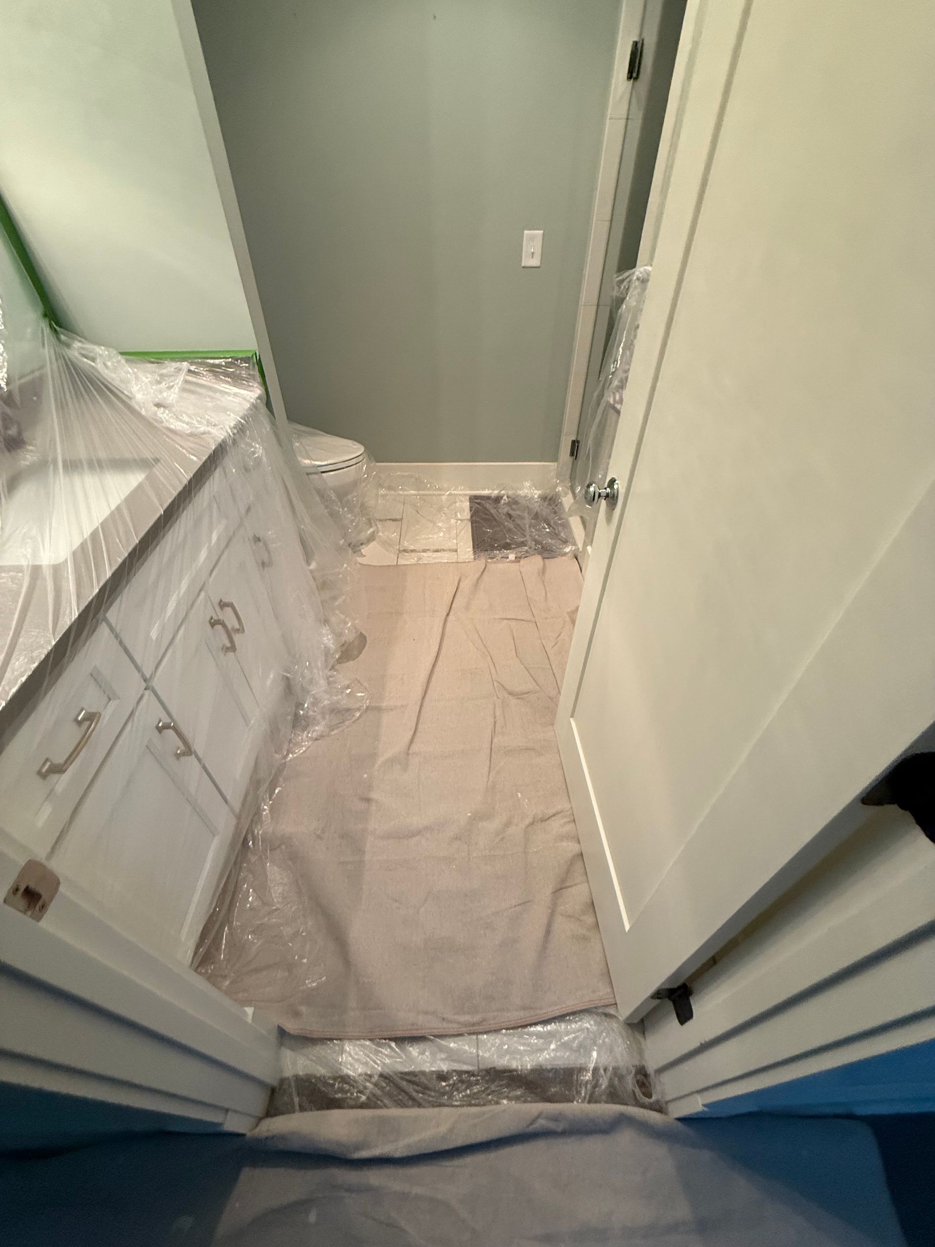 Bathroom renovation with protective covering on floor and countertops, white cabinets, gray wall.