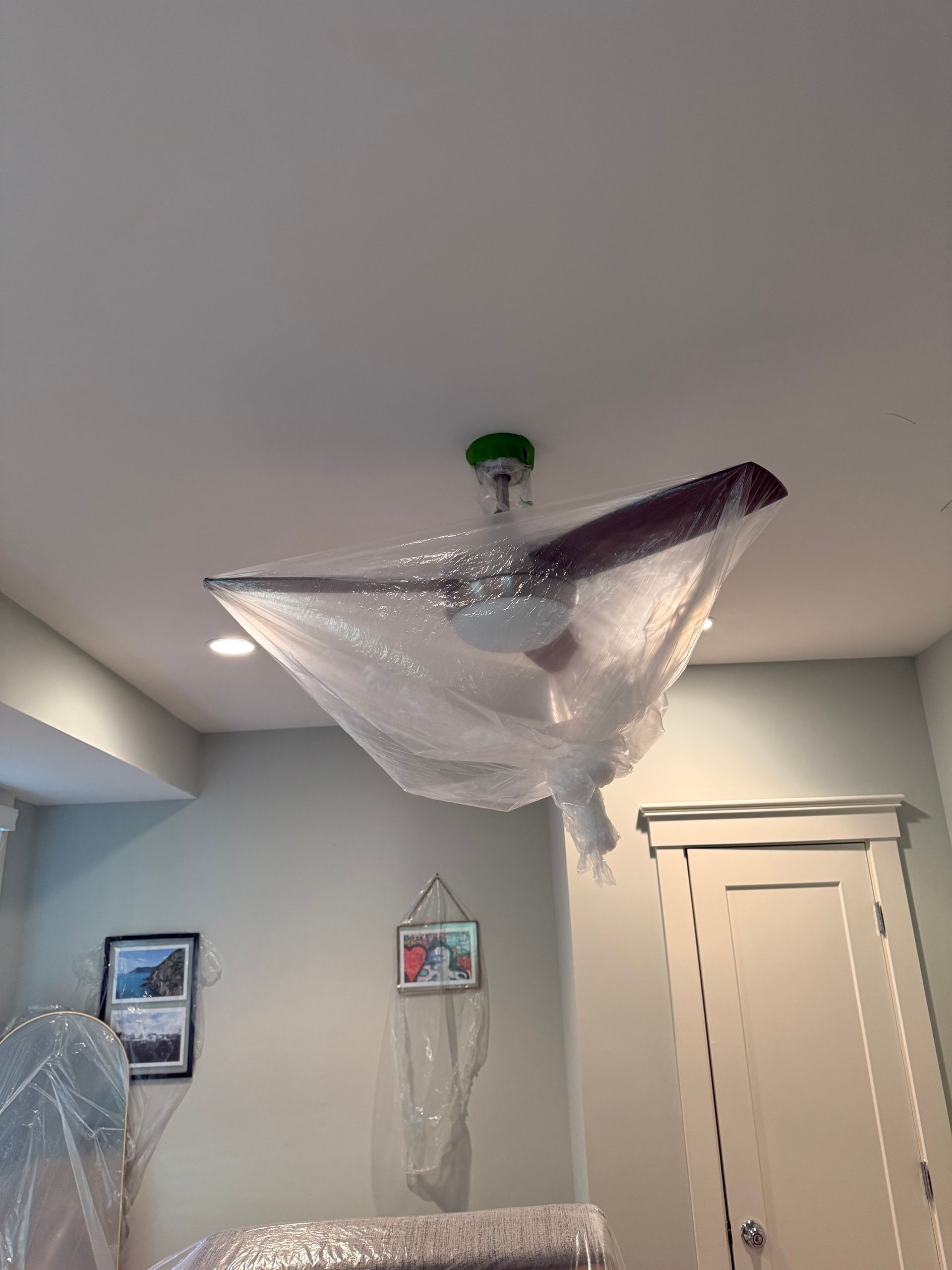 Ceiling fan wrapped in protective plastic. Green ceiling mount, brown blades, and white lights.