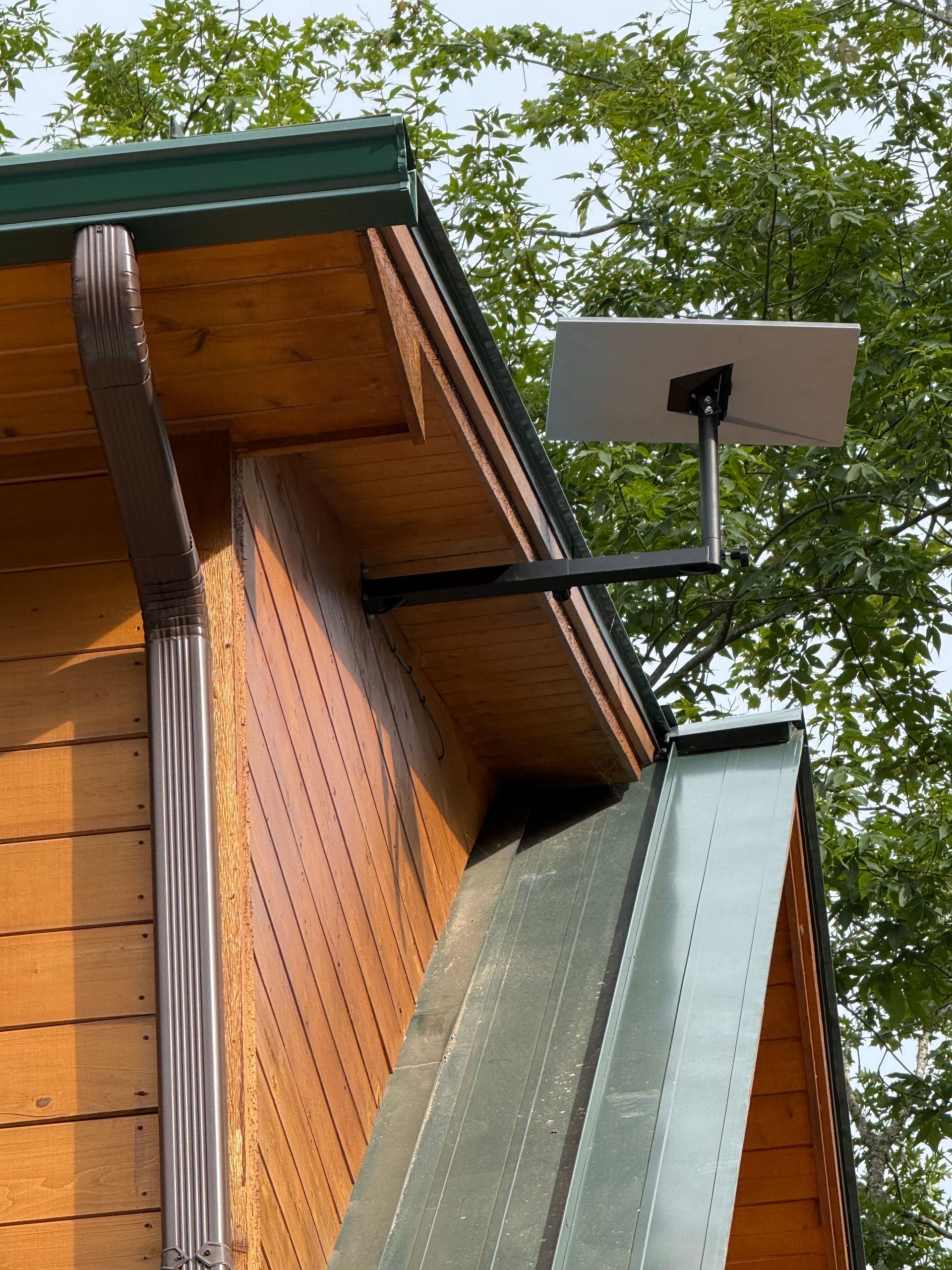 A small, white Starlink internet dish mounted on a black arm attached to a wooden building's roof.