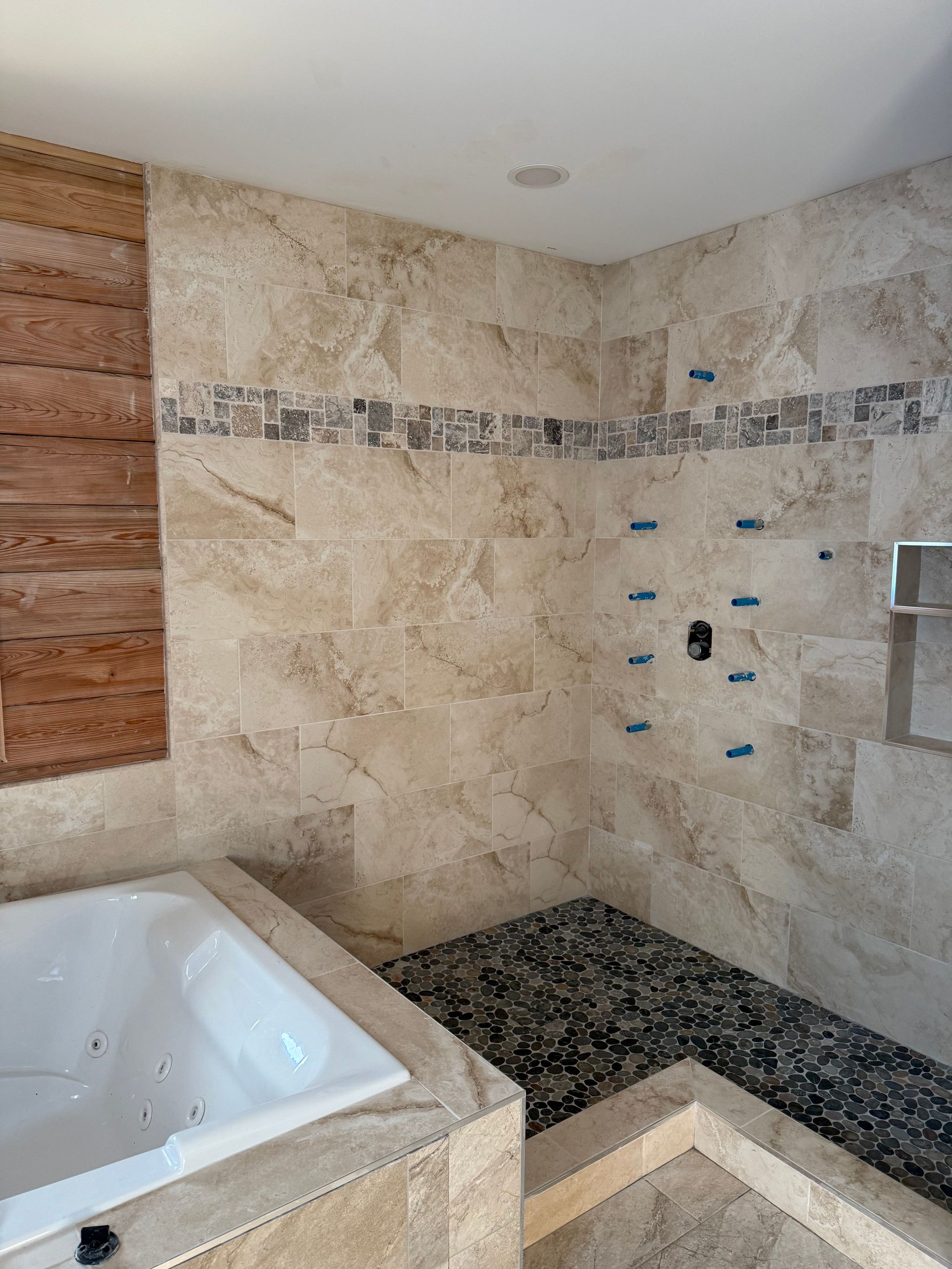 Bathroom with tiled walls and floor, a bathtub, and a shower with river rock flooring.