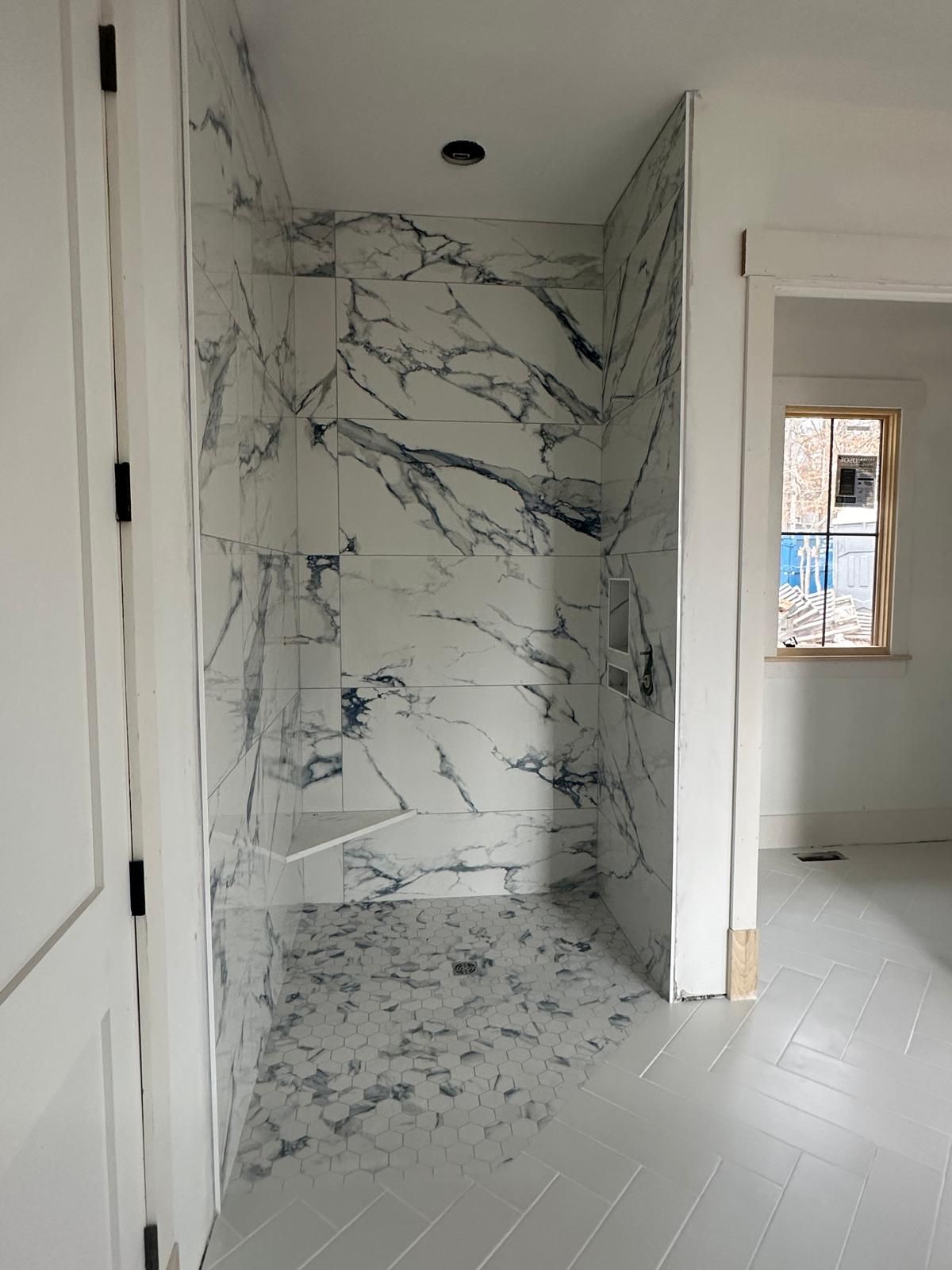 White marble shower stall with glass door, in a room with white walls and floor.