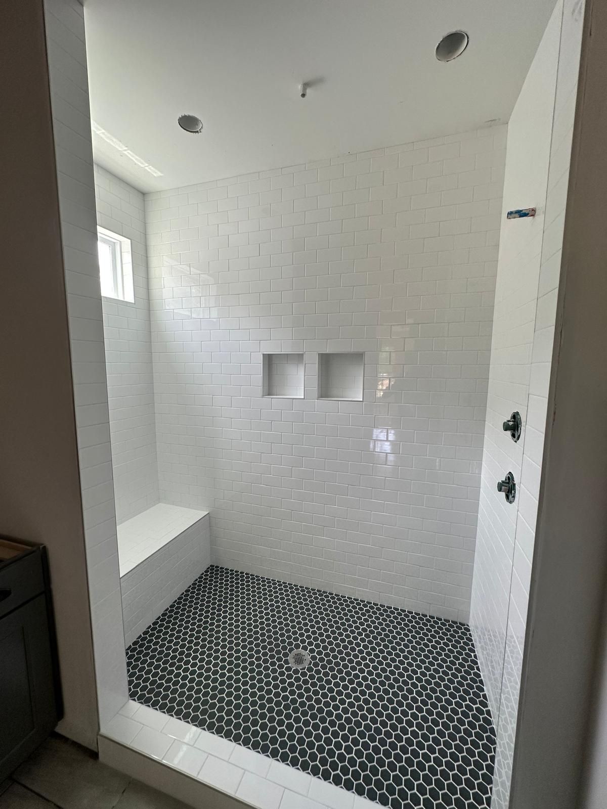 White-tiled shower with a black honeycomb tile floor and a built-in bench.