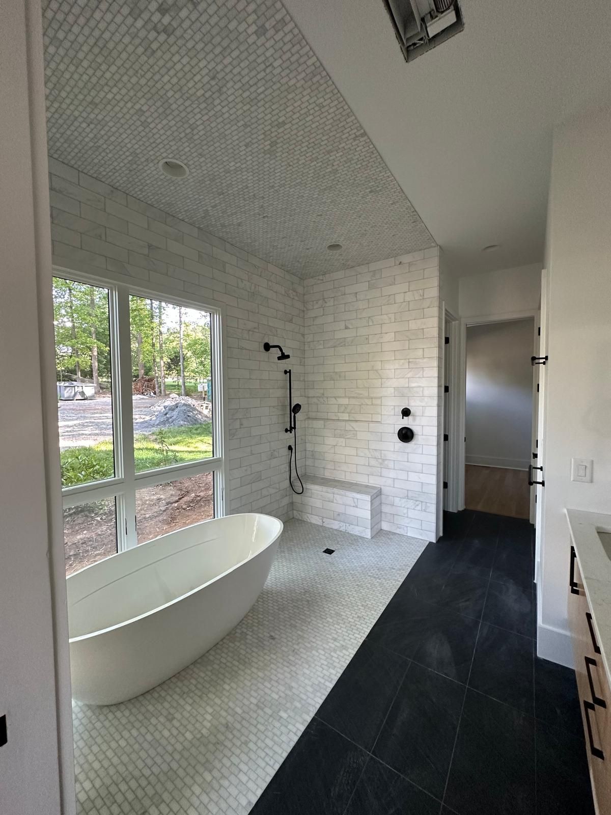 Modern bathroom with bathtub by window, shower, black fixtures, penny tile, dark flooring.