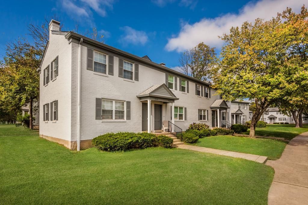 A white house with a lush green lawn and trees in front of it.