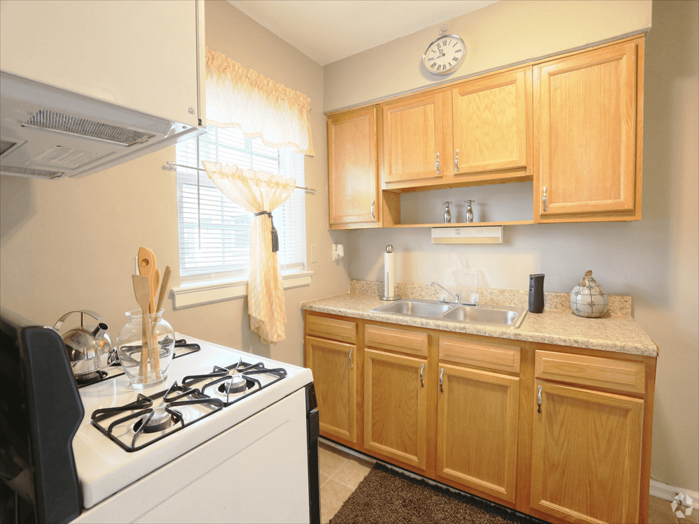 A kitchen with wooden cabinets , a stove , a sink and a window.