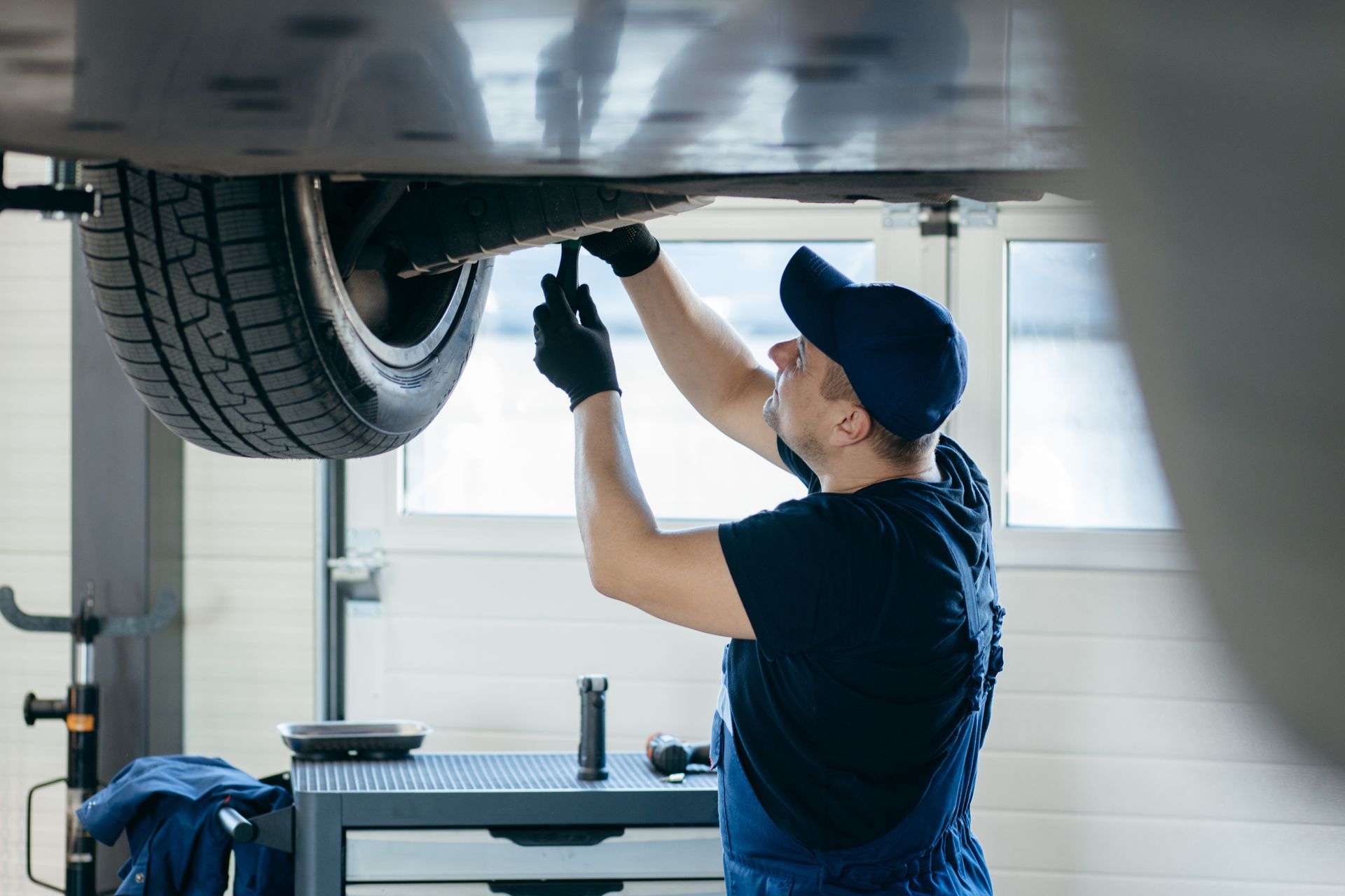 A man is working under a car on a lift in a garage.