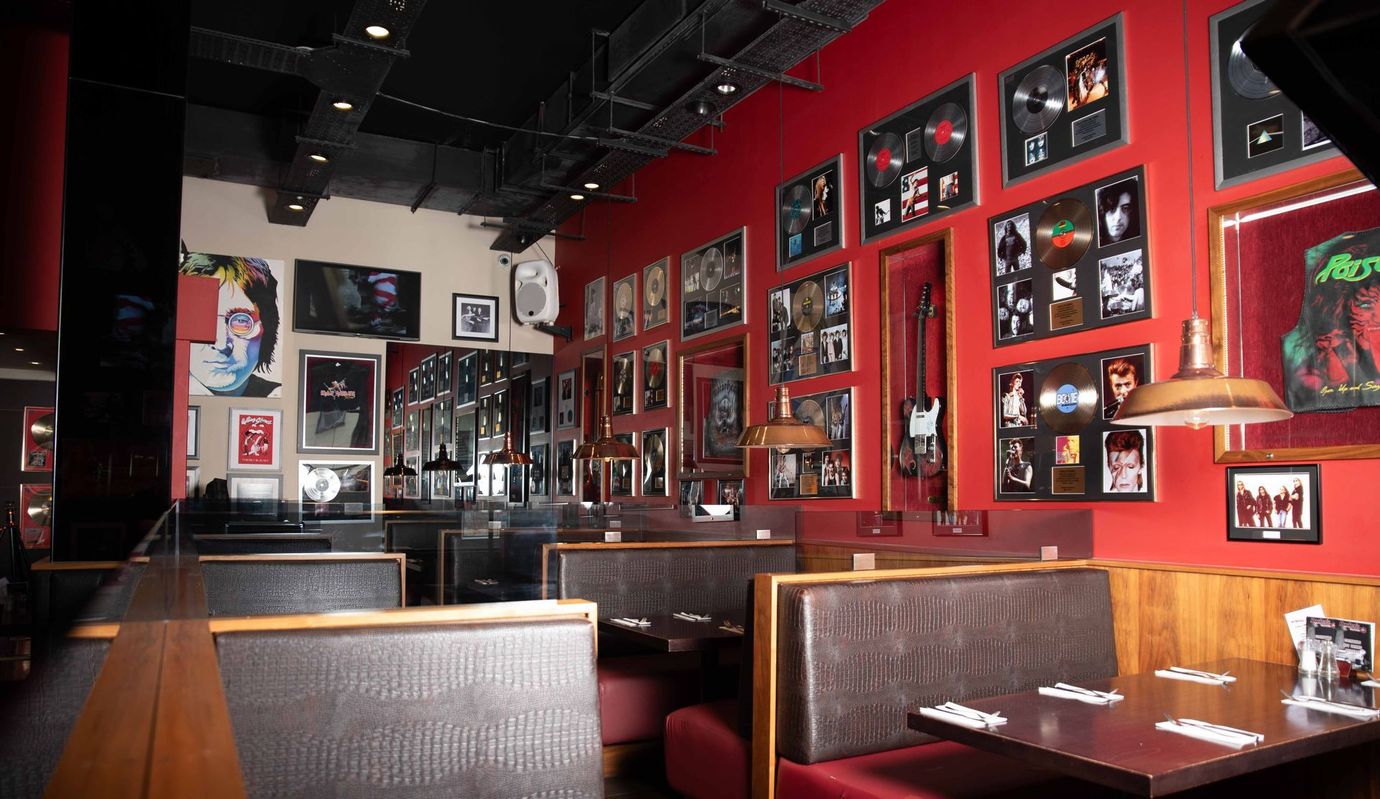Interior of a Hard Rock Cafe restaurant. Red walls adorned with framed music memorabilia, booth seating, and tables set for dining.