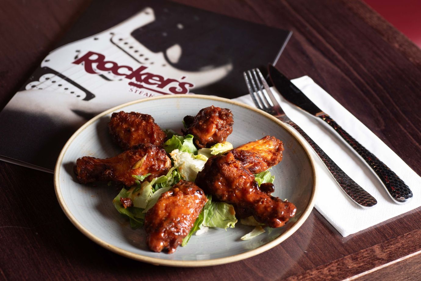 A plate of fried chicken wings on a bed of lettuce, with Rocker's Steakhouse menu and silverware.