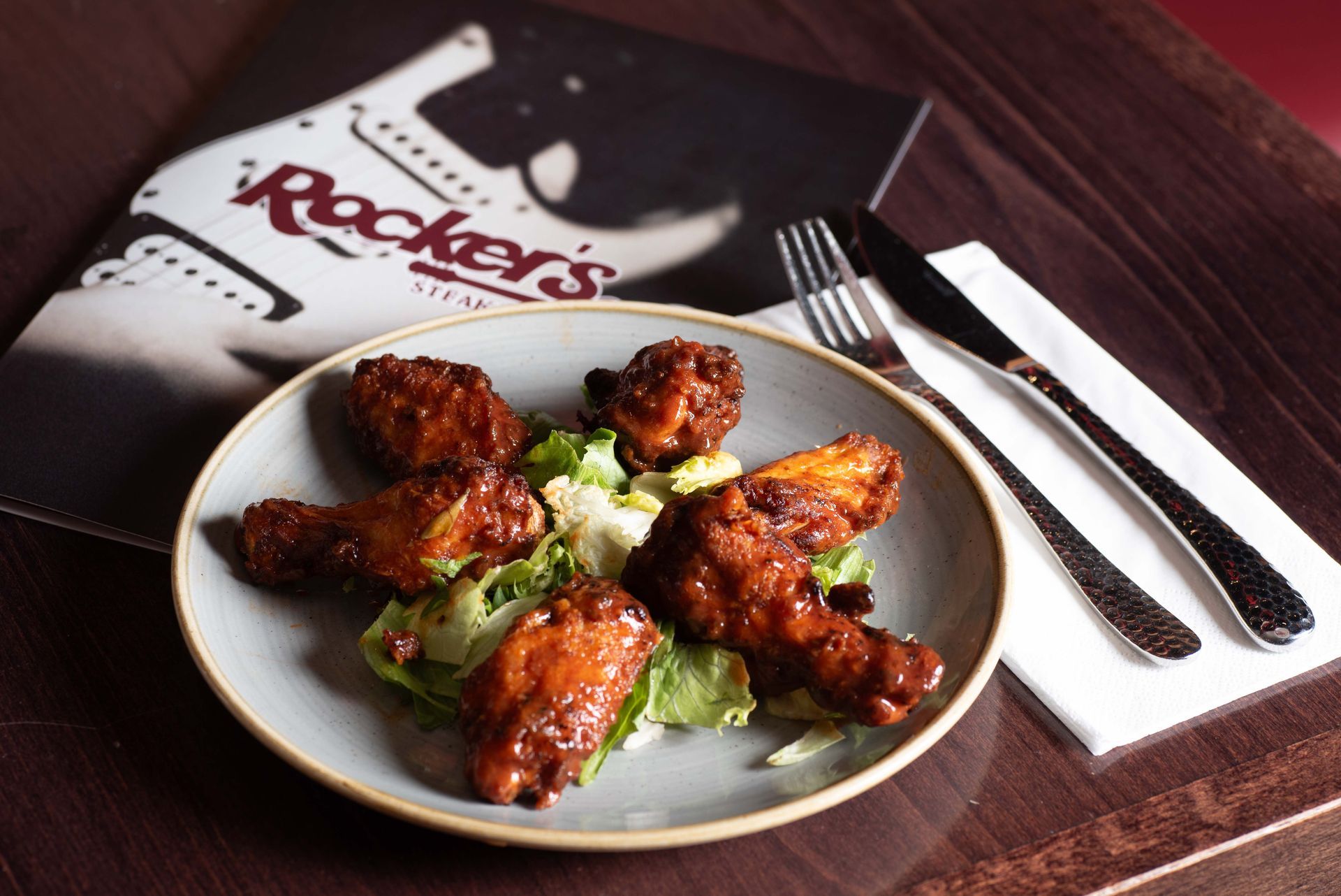 A plate of fried chicken wings on a bed of lettuce, with Rocker's Steakhouse menu and silverware.