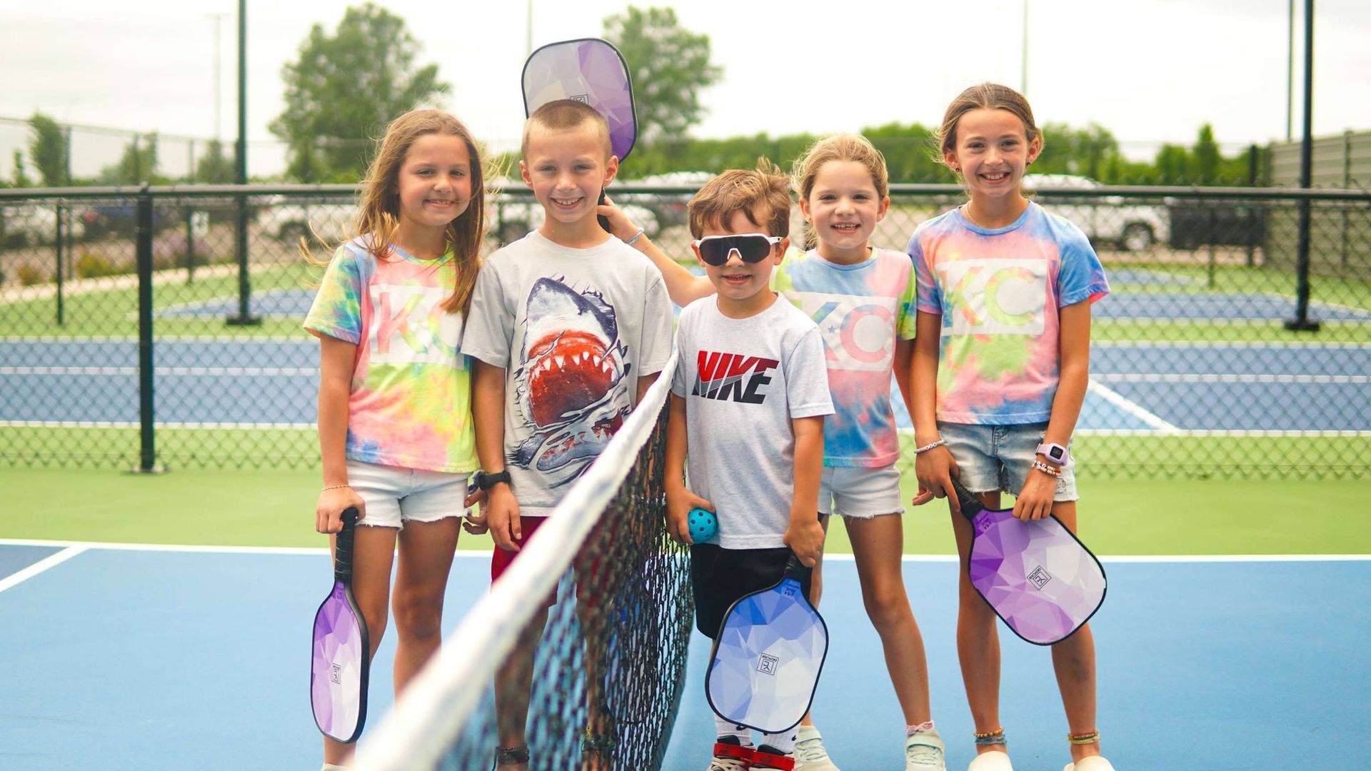 A group of children are posing for a picture on a tennis court.