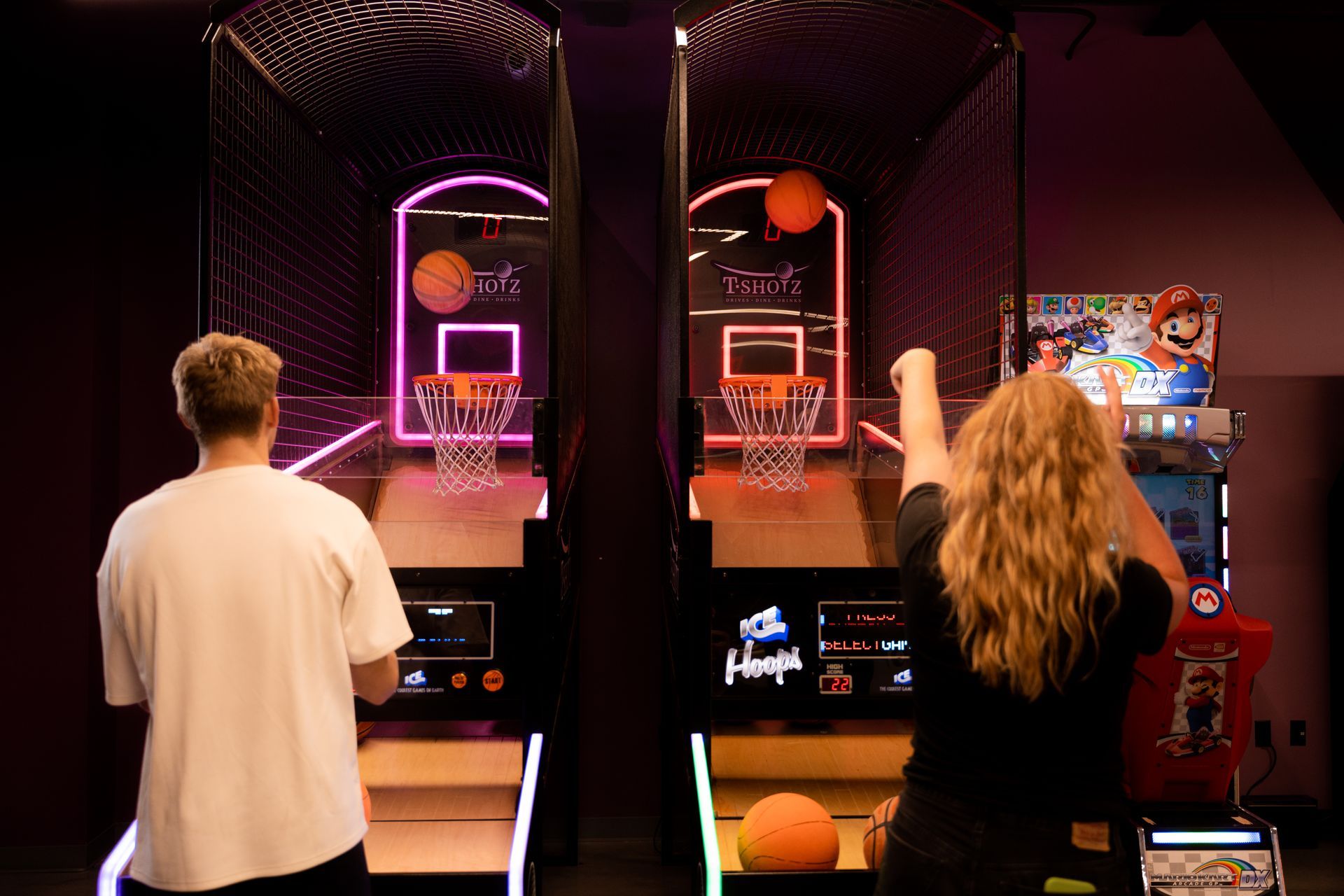 A man and a woman are playing a basketball game in an amusement park.