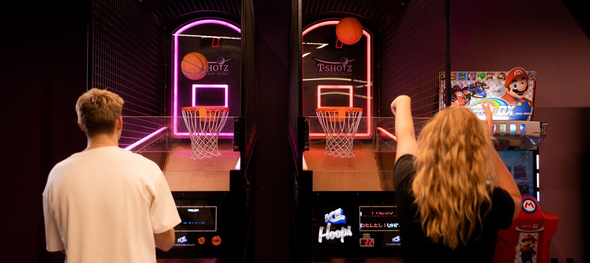 A man and a woman are playing a basketball game in an arcade.