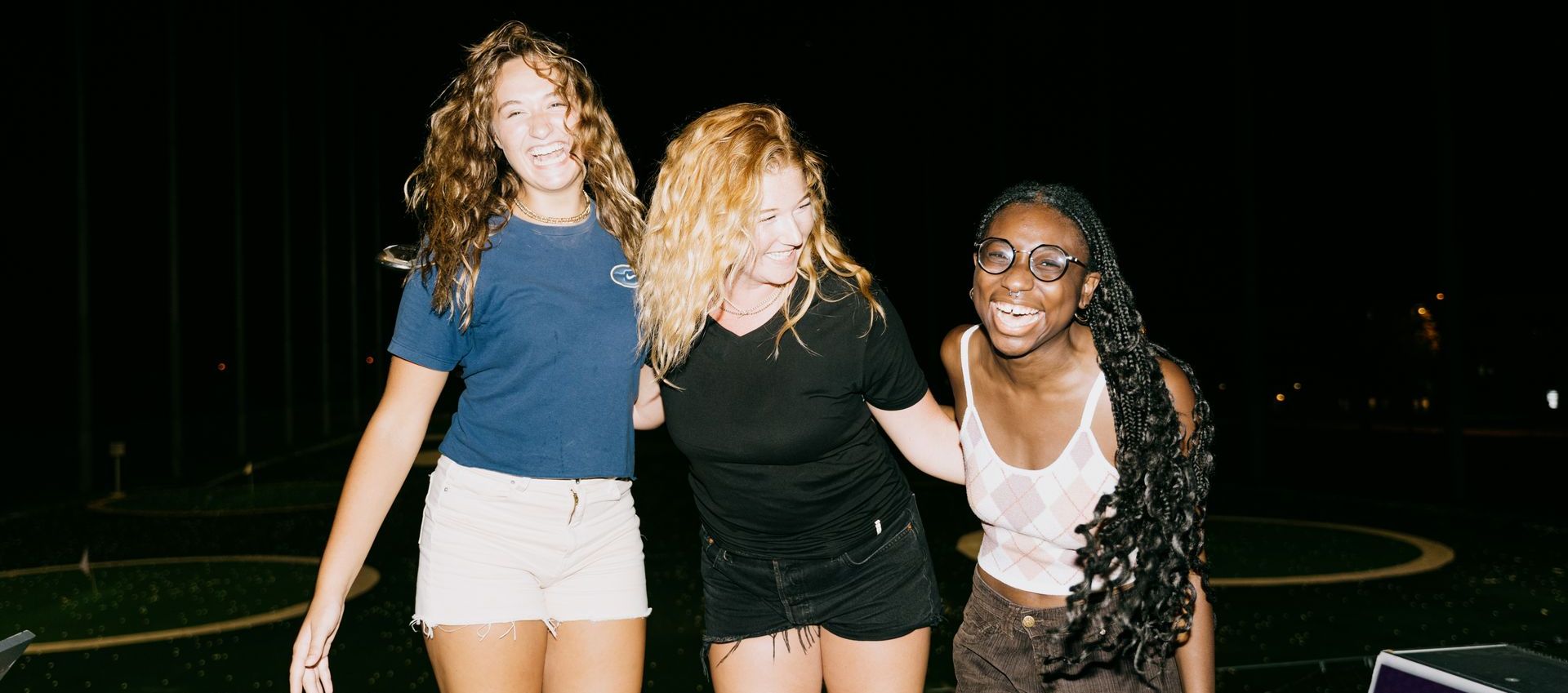 Three young women are posing for a picture together at night.