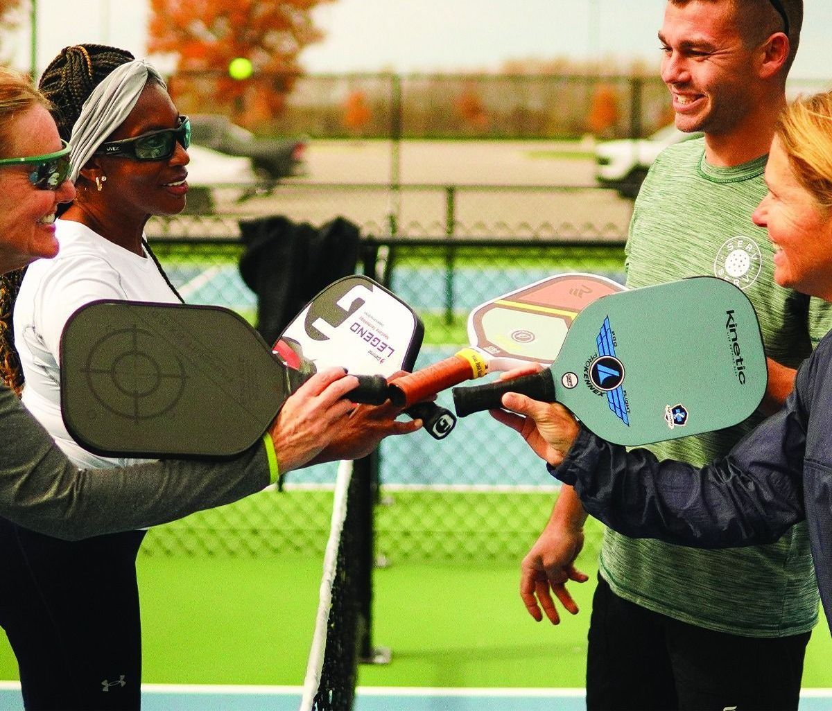 A group of people are holding paddle rackets on a tennis court.