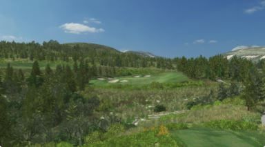 A golf course in the middle of a forest with mountains in the background.