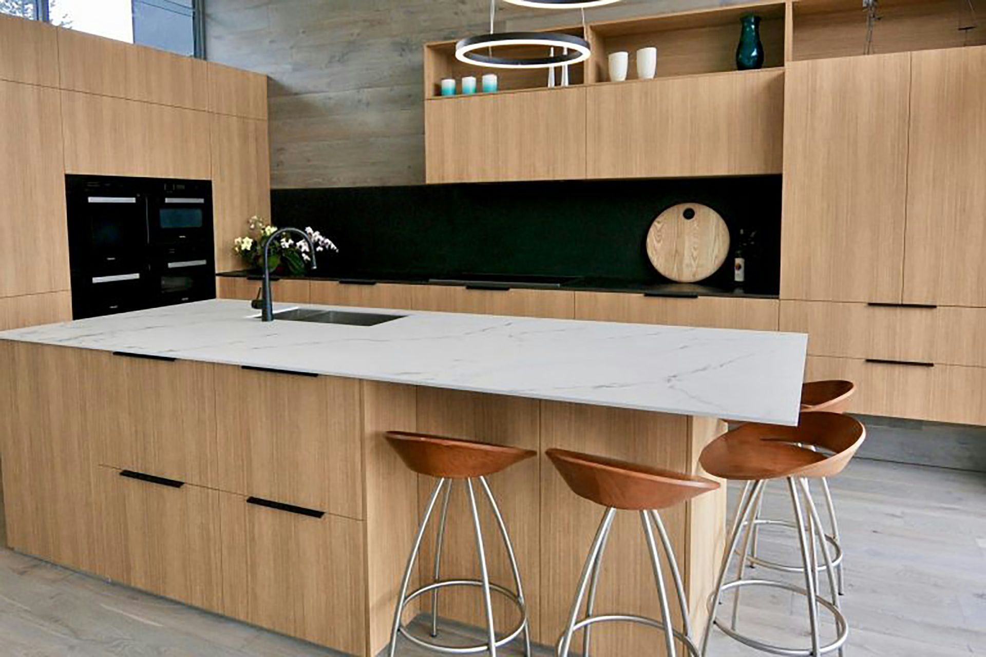 Modern kitchen with light wood cabinets, white island, and three bar stools