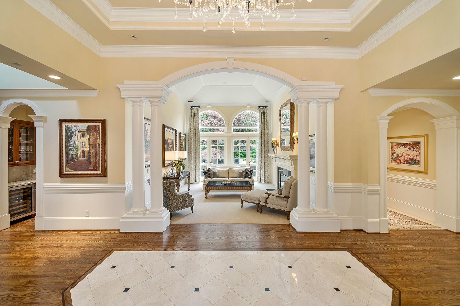 Elegant foyer with white columns, chandelier, hardwood floors, and a seating area beyond an arched entryway