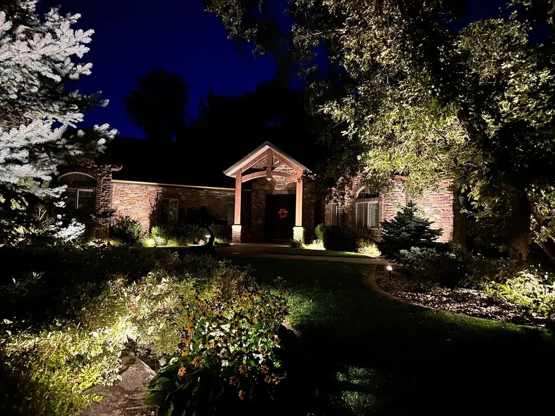 A house is lit up at night with lots of trees in front of it.