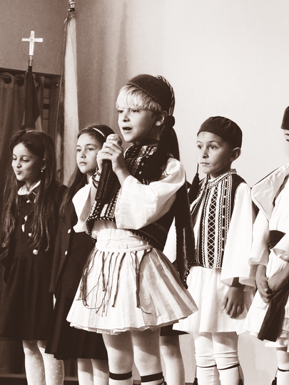 Children performing onstage, with one child singing into a microphone in traditional costumes.