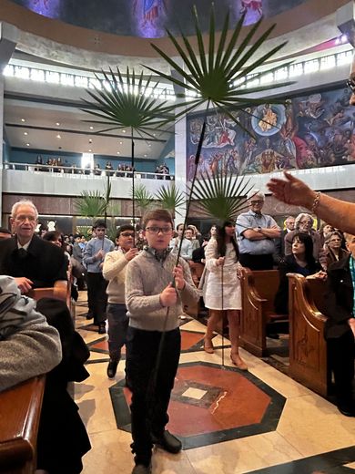 Boy stands in a church aisle with people seated around him during a service