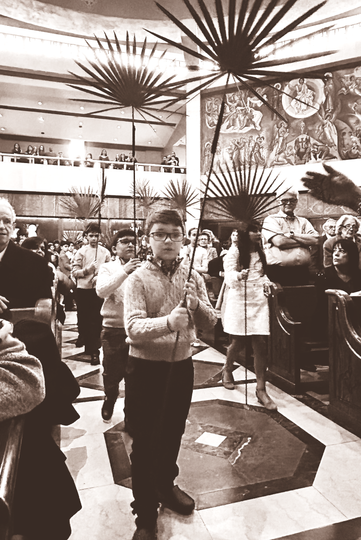 People standing in a busy indoor hall with decorative starburst ceiling lights and a wall clock.